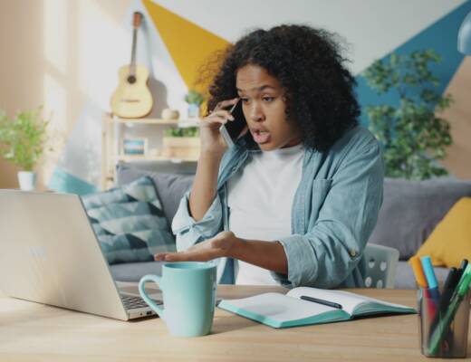 Young woman talking on phone at laptop desk; unmet needs