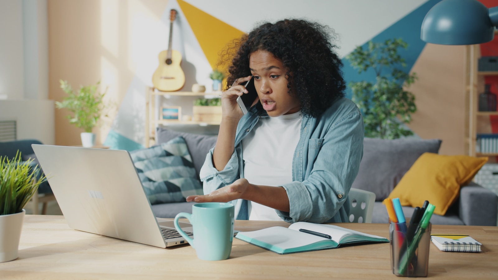 Young woman talking on phone at laptop desk; unmet needs