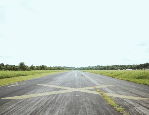 gray road surrounded by green grass during daytime; extend runway