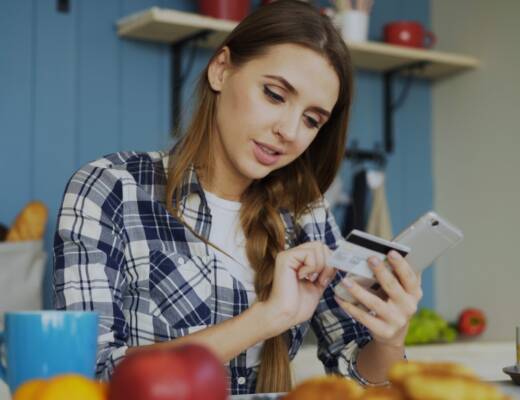 Woman using credit card with smartphone at table; Financial Habits