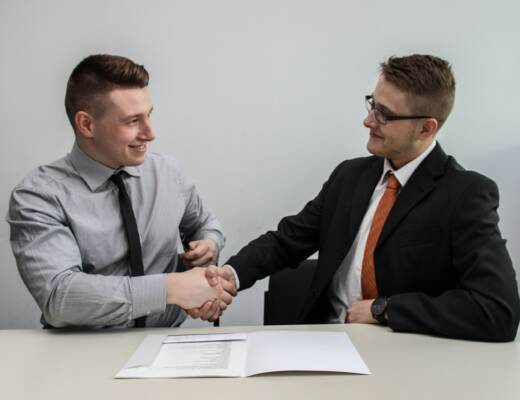 two men facing each other while shake hands over business operating agreement.