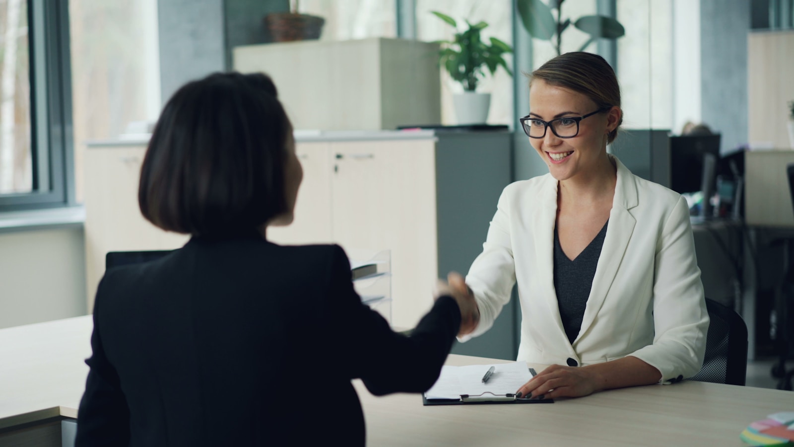 Two women shaking hands across a desk; questions before hiring employee