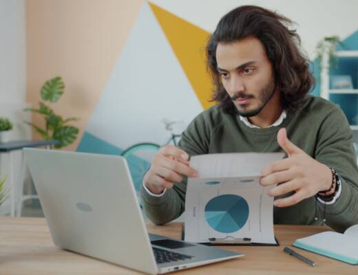 Man looking at laptop and paper in colorful room; founders confuse lean cheap