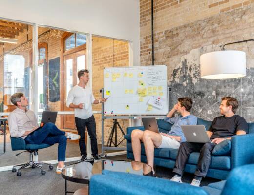 three men sitting while using laptops and watching man beside whiteboard; building in public