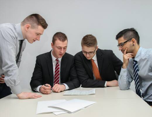 four men meeting in conference room reviewing financial documents together; accidentally destroy investor trust