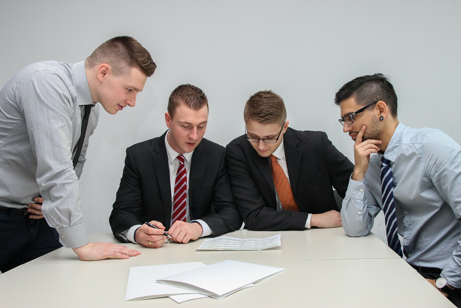 four men meeting in conference room reviewing financial documents together; accidentally destroy investor trust