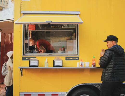 man in black jacket standing by yellow food truck; growing food truck empire