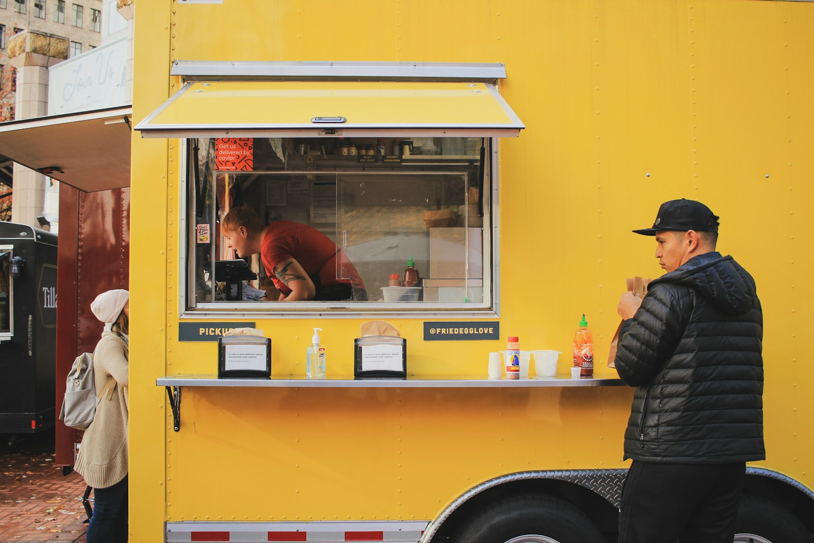 man in black jacket standing by yellow food truck; growing food truck empire